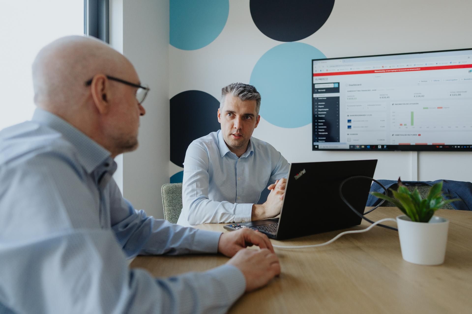 Twee mannen in overleg over digitale boekhouding met dashboard op scherm, moderne kantooromgeving