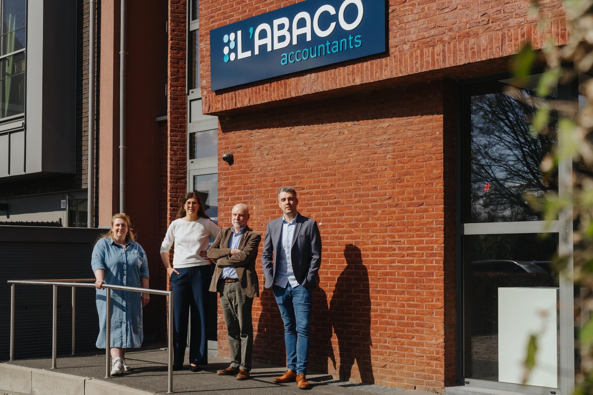 Team van L'Abaco Accountants poseert buiten voor kantoorgebouw met logo, klaar om klanten te ontvangen